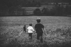 Black and white photograph of three boys running away from the camera in a field